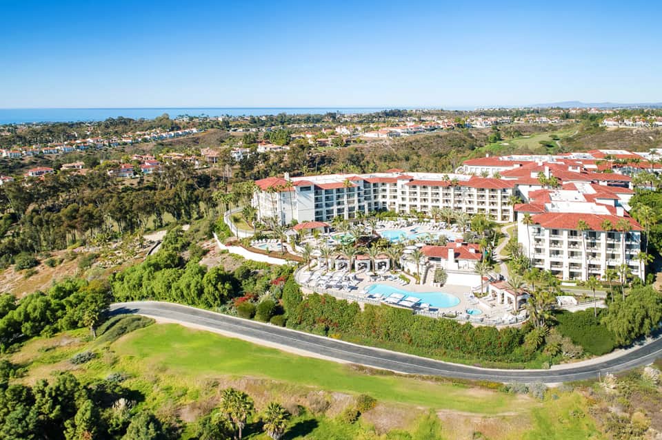 Aerial view of hillside resort with red-roofed buildings, pools, and coastal landscape