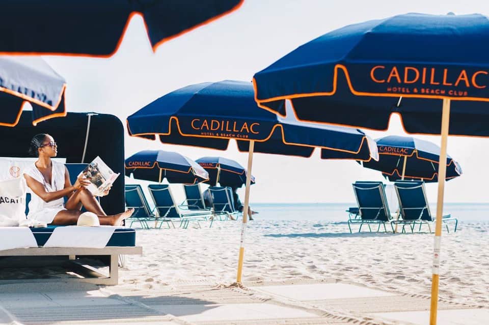 Woman relaxing on beach under branded Cadillac umbrellas with beach chairs and ocean