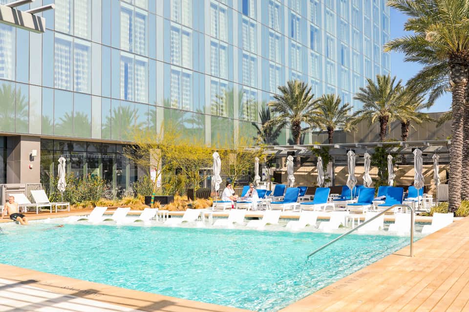 Resort pool with turquoise water, white lounge chairs, and modern high-rise building