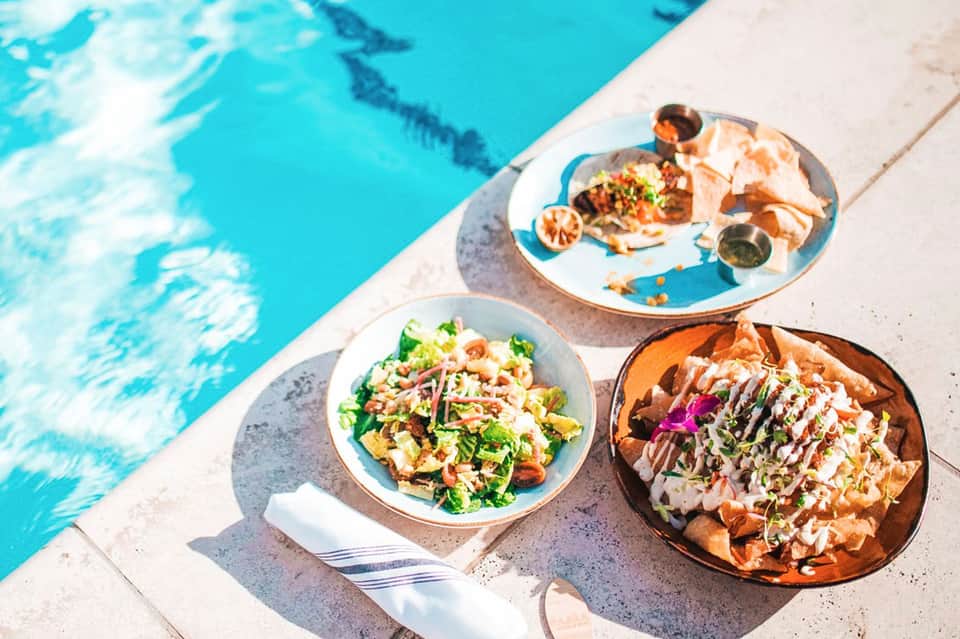 Colorful dishes of food and appetizers on pool deck next to turquoise swimming pool