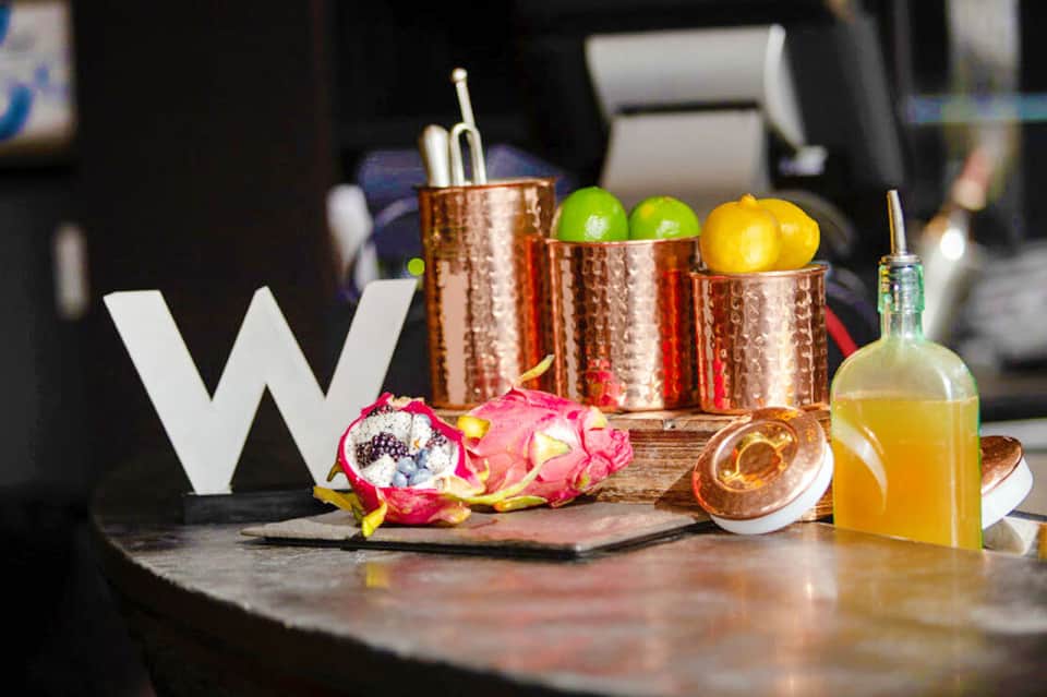 Luxury cocktail bar display with copper mugs, fresh citrus fruits, tropical flowers, and bottled mixers on dark marble counter
