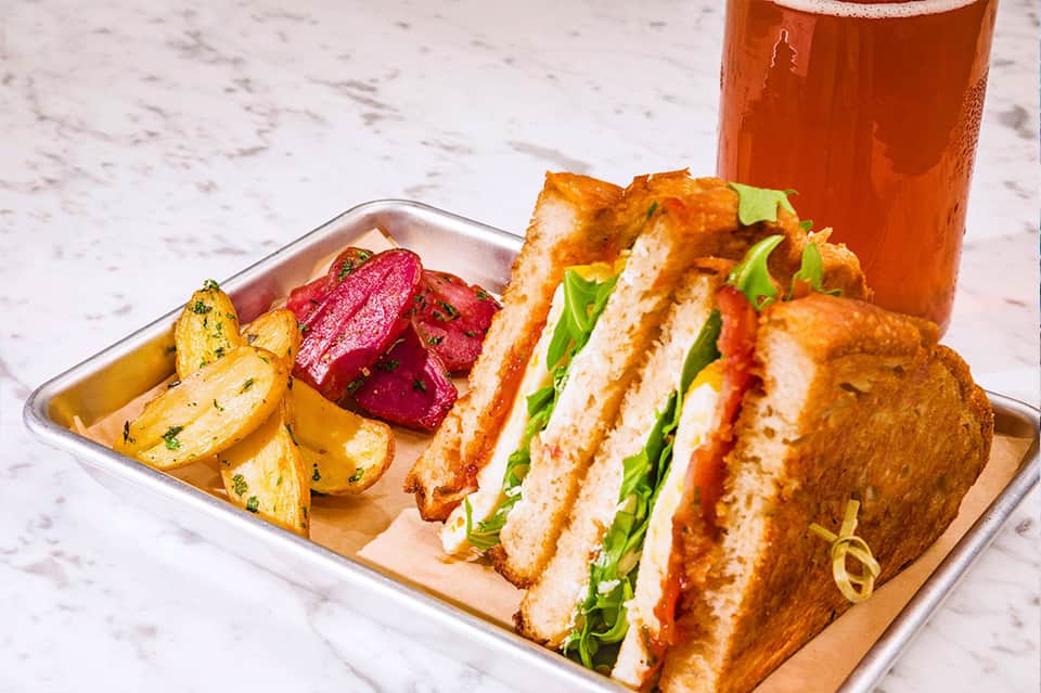Gourmet sandwich with bacon, tomato, and lettuce served with potatoes and beverage