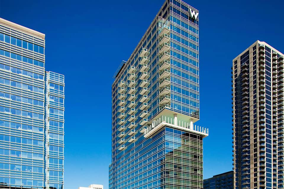 Modern high-rise hotel towers with glass facades and green balconies under clear blue sky