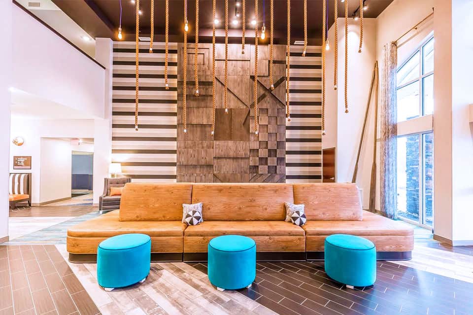 Modern hotel lobby with large wooden sofa, turquoise ottoman seating, and striped accent wall
