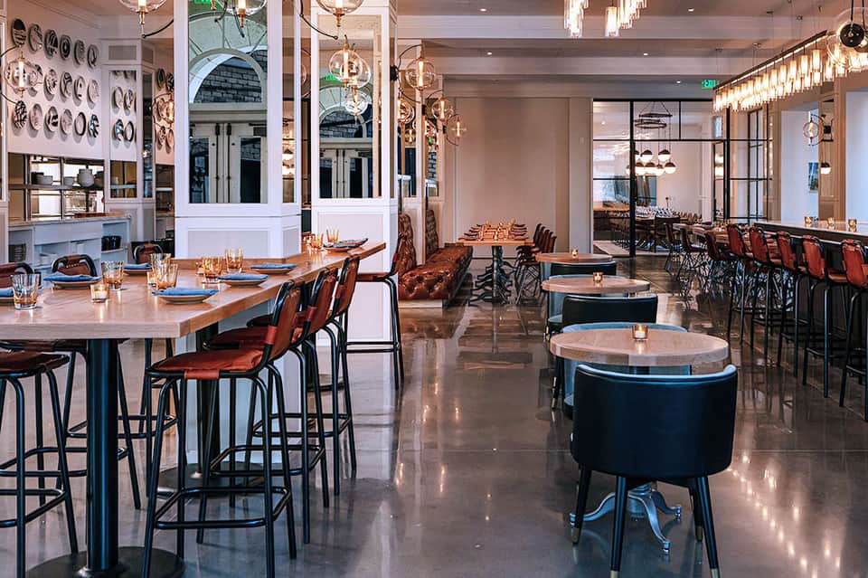 Modern restaurant interior with wood tables, bar seating, pendant lighting, and decorative wall plates