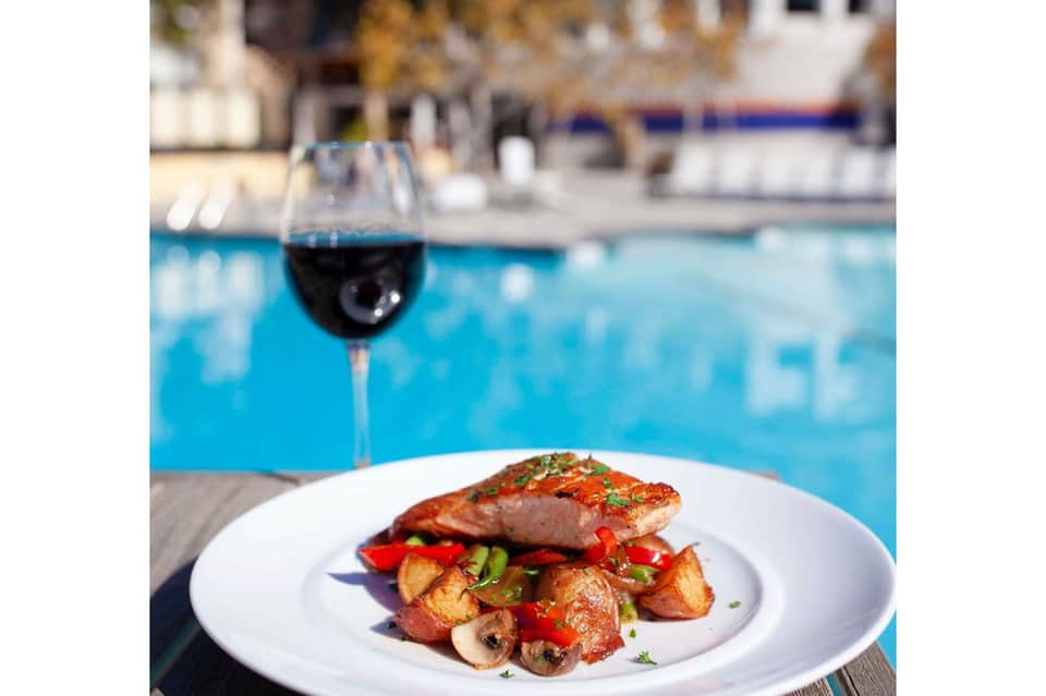 Gourmet salmon dish with roasted vegetables and wine by an outdoor pool