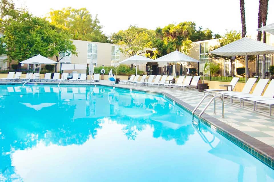 Resort swimming pool with crystal blue water, lounge chairs, white umbrellas, and palm trees