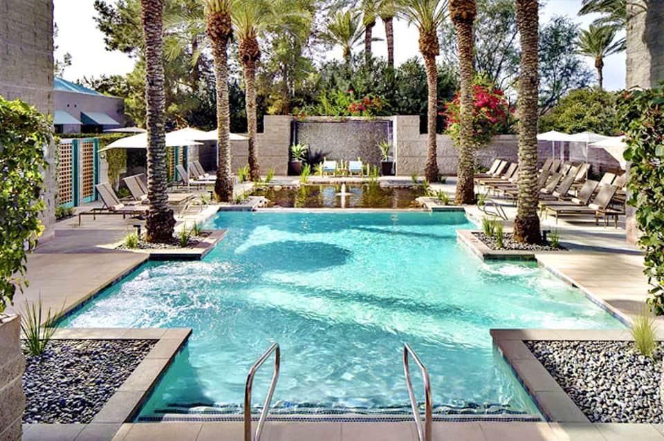 Luxury resort pool with turquoise water, palm trees, loungers, and modern concrete architecture