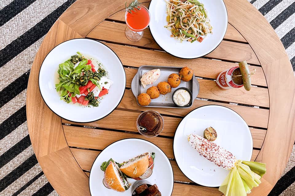 Overhead view of wooden table with five plated dishes, cocktail, and appetizers