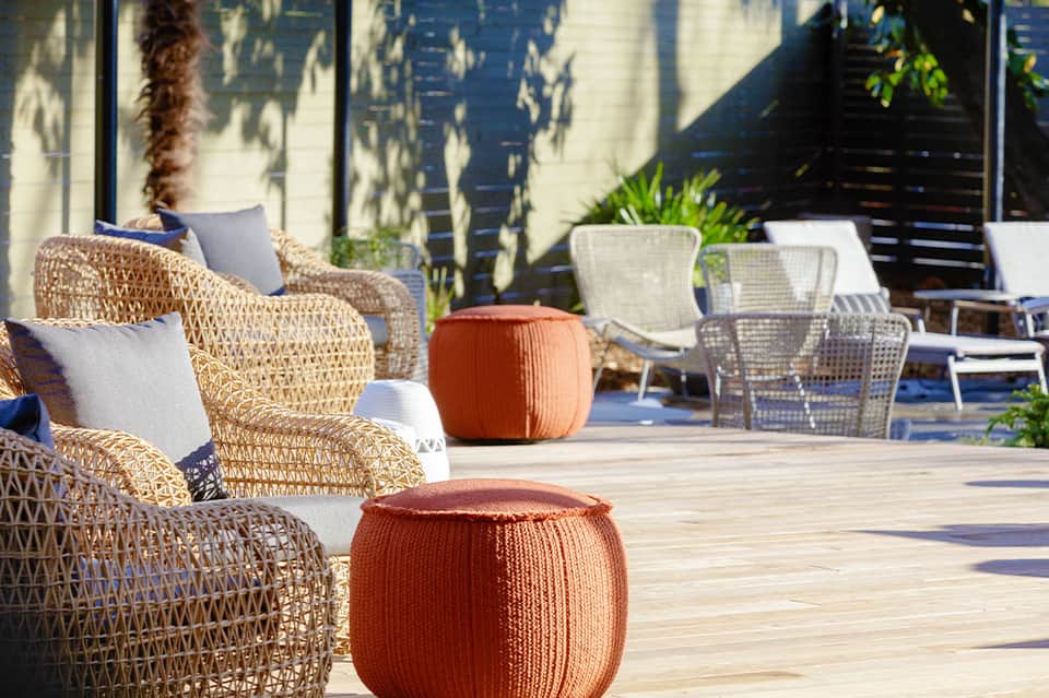 Woven lounge chairs and orange poufs on sunny wooden deck with white modern architecture