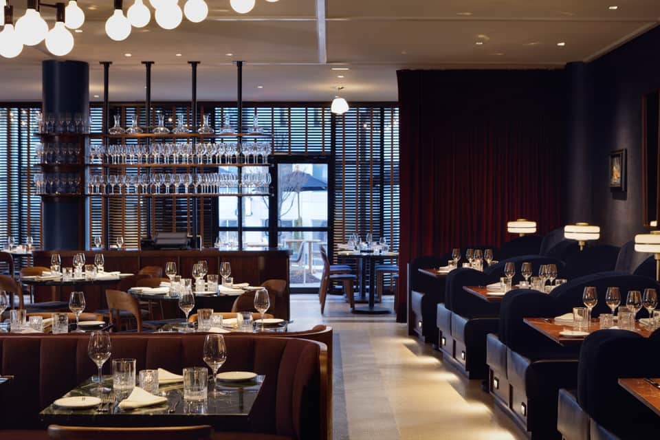 Upscale restaurant dining room with dark wood tables, modern bar, and ocean views