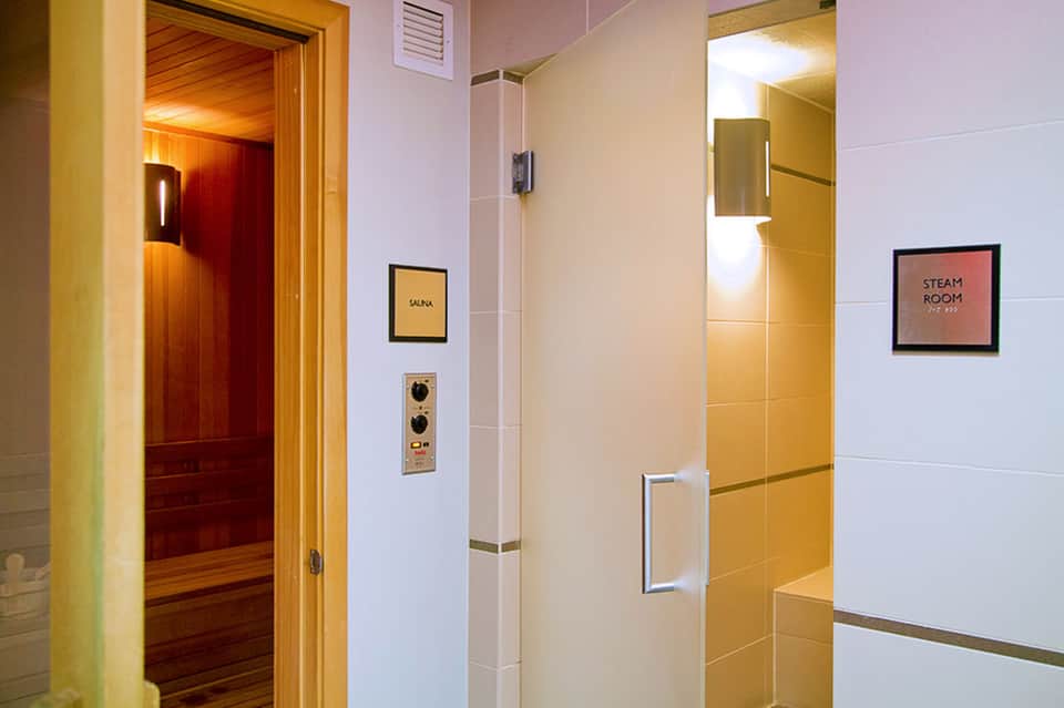 Hallway with sauna and steam room entrance doors, wooden sauna visible through open door