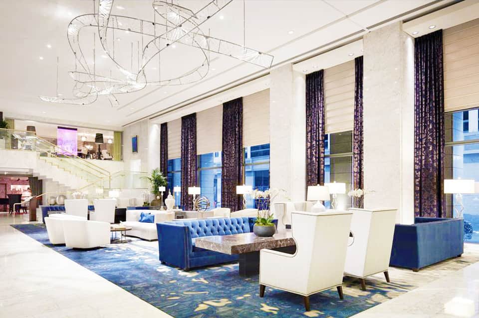 Modern hotel lobby with blue velvet seating, white chairs, dark curtains, and contemporary chandelier