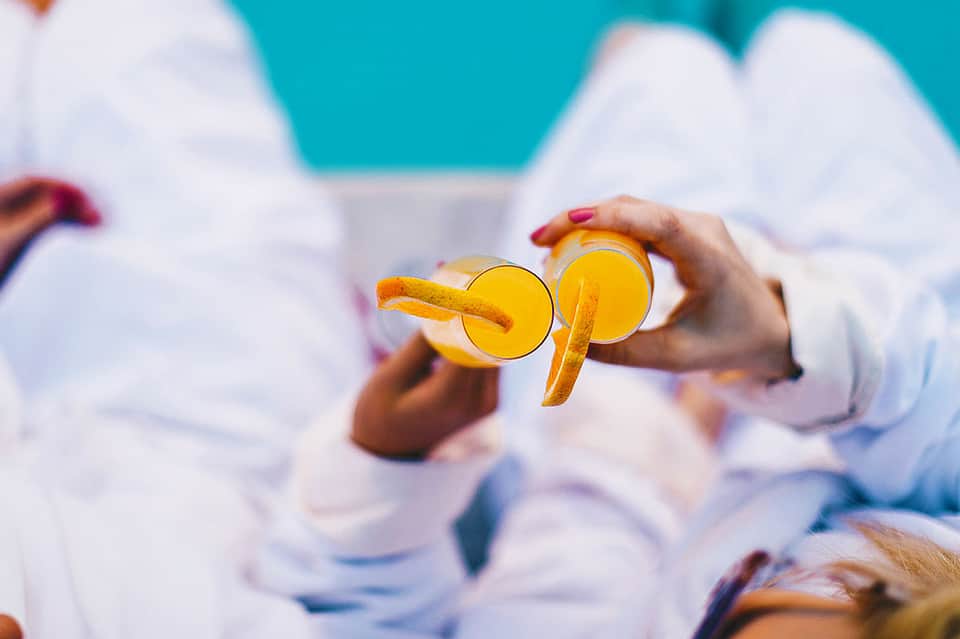 Hands holding two glasses of fresh orange juice with orange slices by the beach