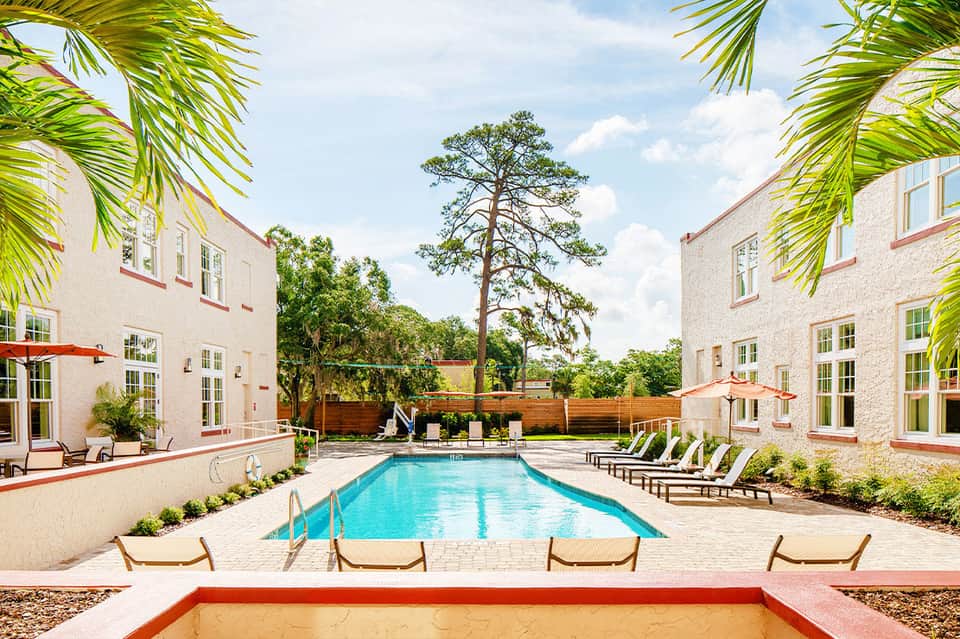 Rectangular swimming pool flanked by cream-colored buildings with palm trees and lounge chairs