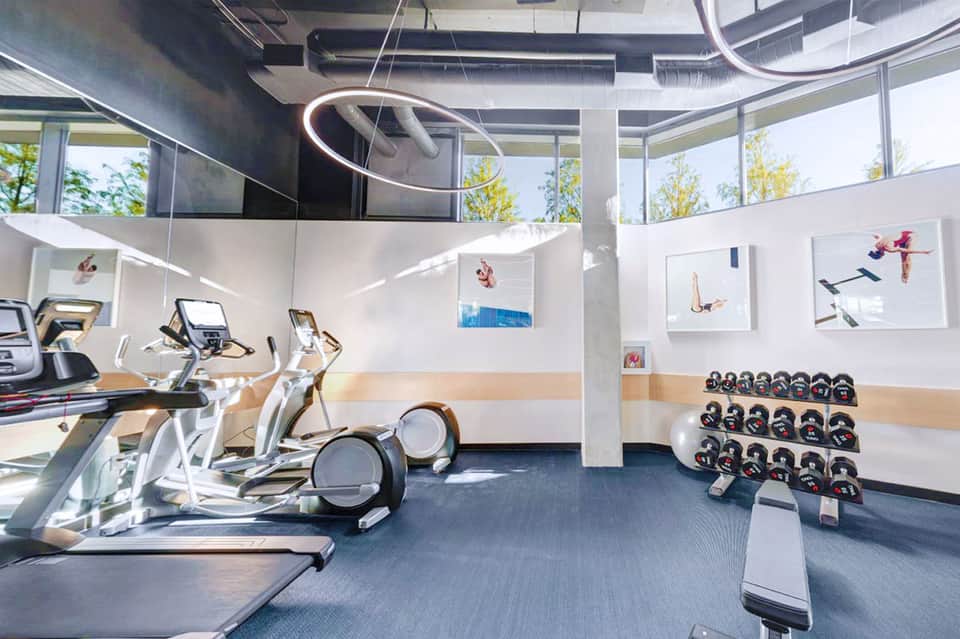 Modern fitness center with cardio equipment, dumbbells, and inspirational wall art with large windows