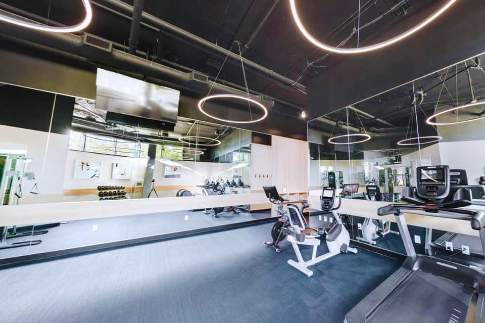 Modern gym interior with cardio equipment, weights, neon circular ceiling lights, and mirrored walls