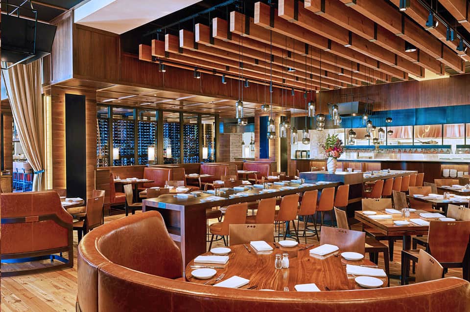 Contemporary restaurant dining room with wood ceiling, burgundy leather booths, and wine storage