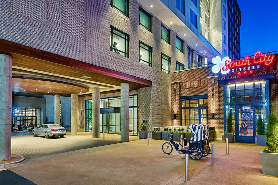Modern urban hotel entrance with brick facade, South City Kitchen sign, and bicycle rickshaw at dusk