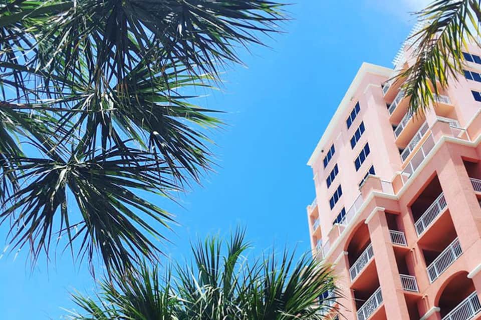 Coral pink hotel building with palm trees against blue sky