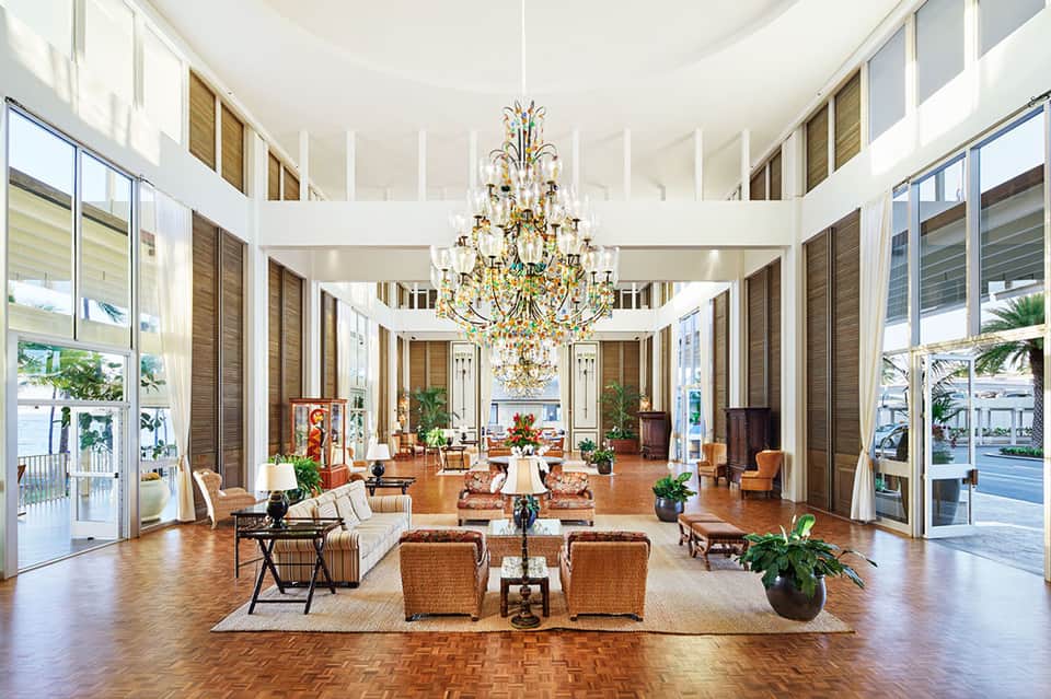 Elegant hotel lobby with high ceilings, ornate crystal chandelier, wicker seating, and large windows