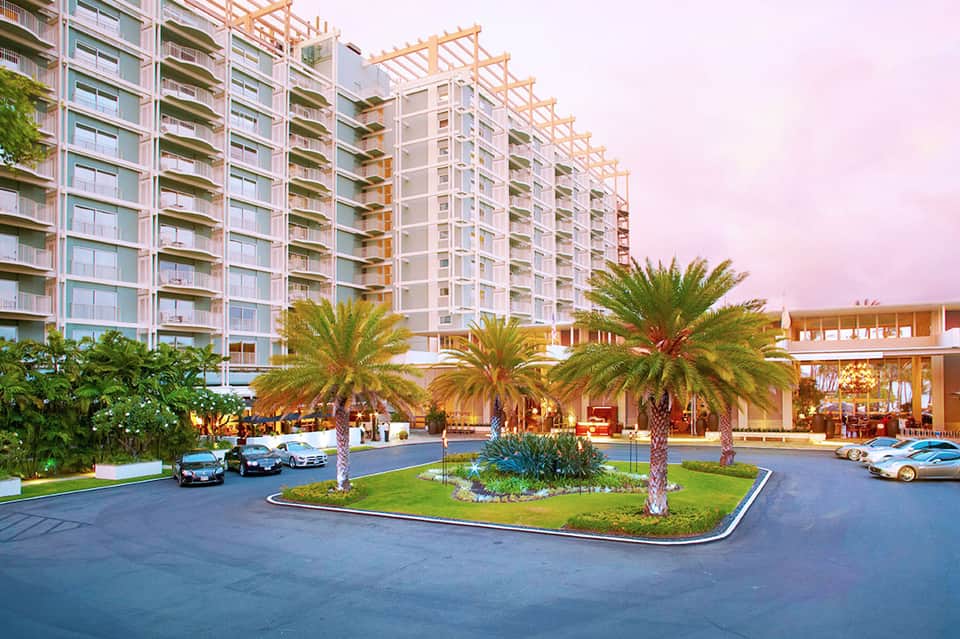 Luxury resort exterior with palm-lined driveway, multi-story residential towers, and manicured landscaping at dusk
