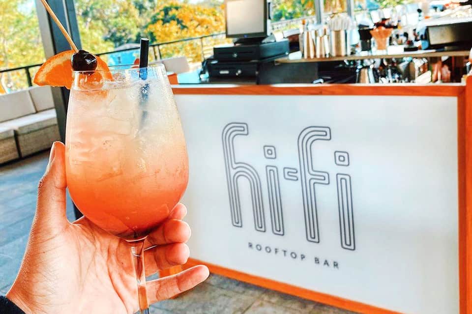 Colorful cocktail with orange slice at rooftop bar overlooking city