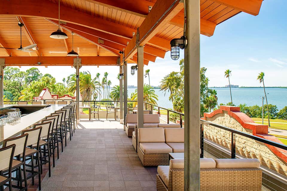 Covered patio bar overlooking bay with palm trees, boats, and blue water views