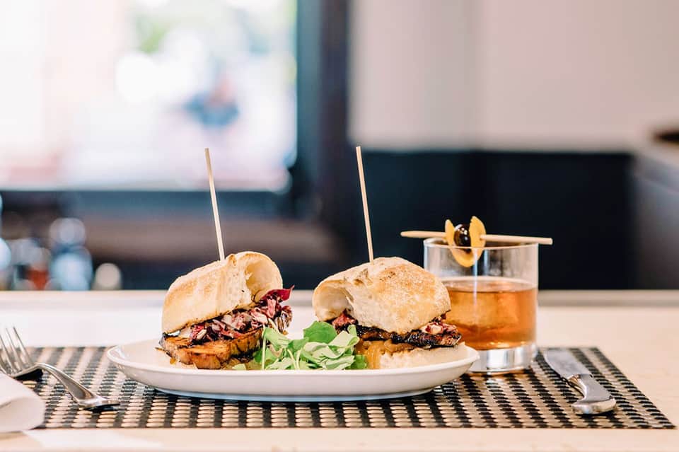 Two gourmet burgers with coleslaw on white plate, served with cocktail and ocean view