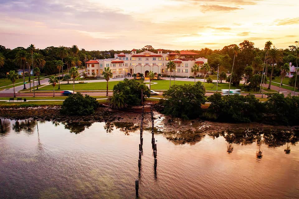 Pink mansion-style resort building at sunset overlooking waterfront with palm trees