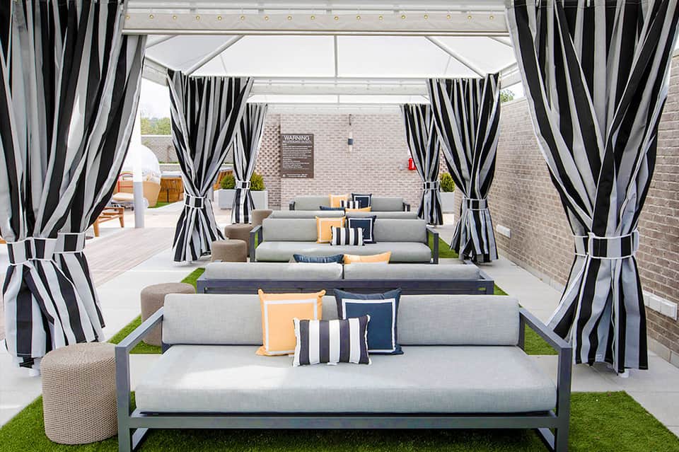Luxury outdoor lounge area with gray sectional sofas, striped black and white curtains, and brick backdrop