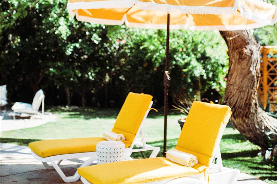 Yellow lounge chairs under umbrella in shaded garden area with trees
