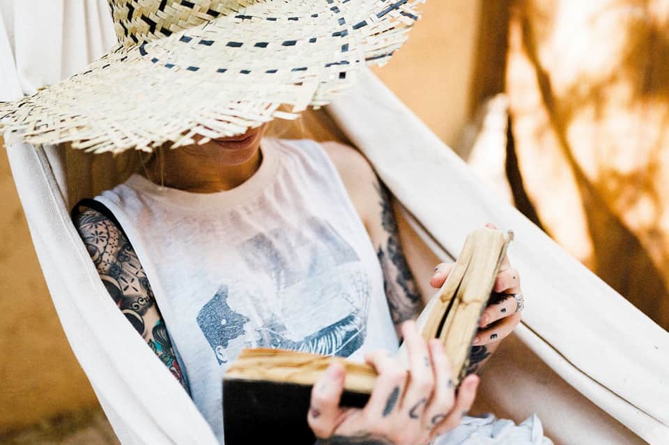 Person in hammock wearing straw hat, reading a book while relaxing outdoors