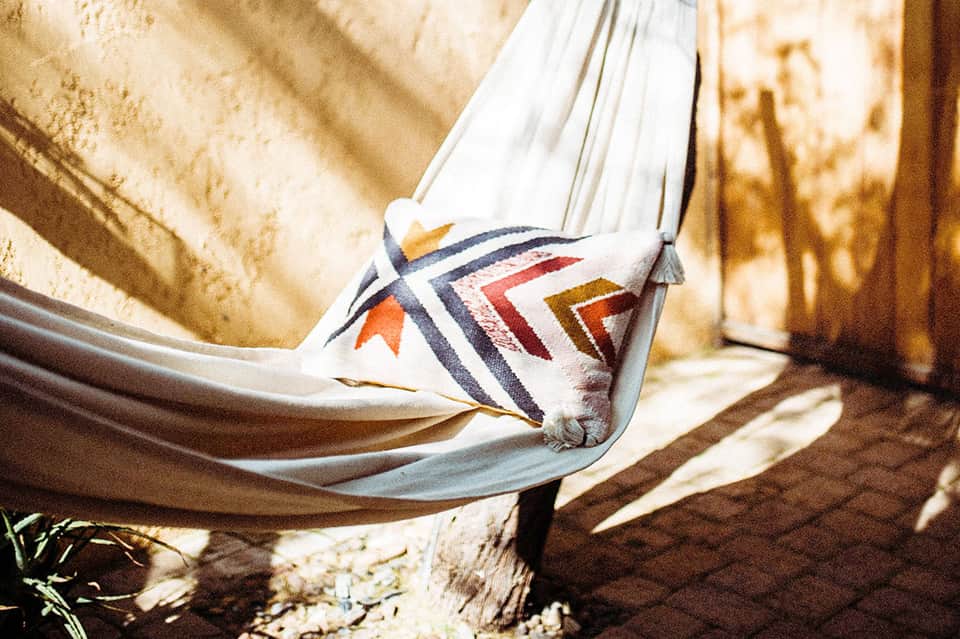White hammock with colorful geometric pattern hanging between wooden posts in sandy area