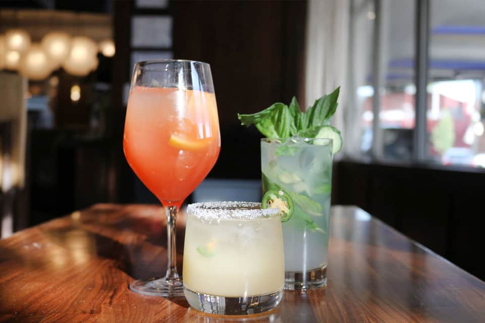 Three colorful cocktails on a bar counter with elegant glassware