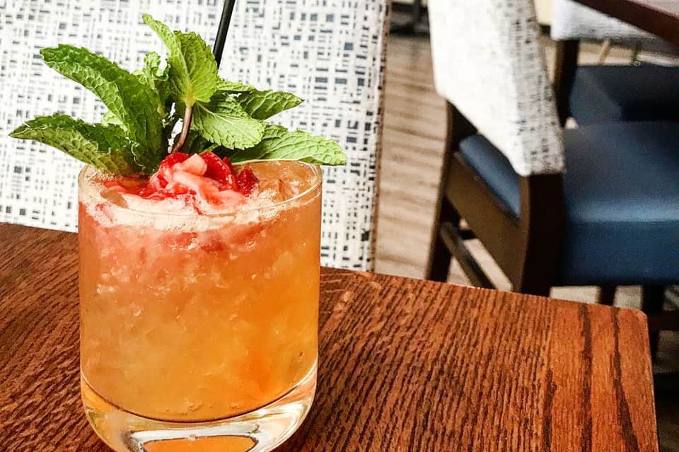 Cocktail with orange liquid, ice, mint garnish, and grapefruit twist on wooden table