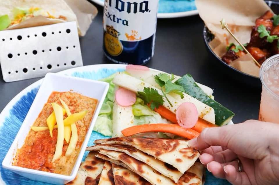 Colorful Mexican appetizers including quesadillas, fresh vegetables, radishes, and salsa with Corona beer