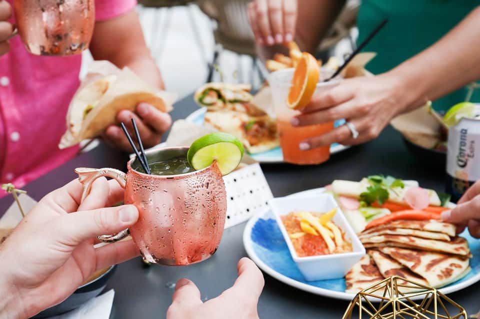 Guests holding cocktails and appetizers at an outdoor social gathering with colorful drinks