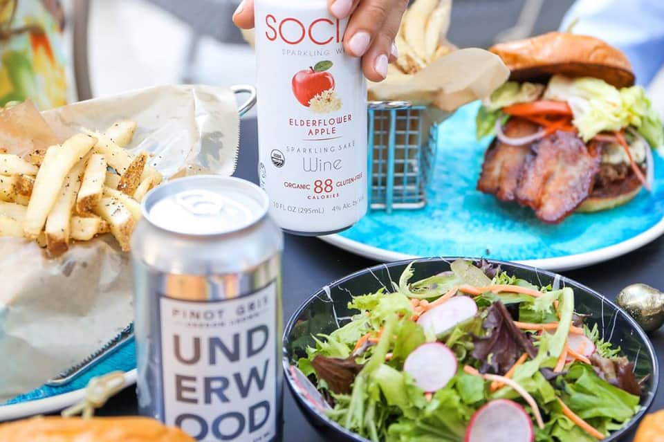 Sparkling wine bottle and beer displayed with gourmet burgers, salads, and fries on table