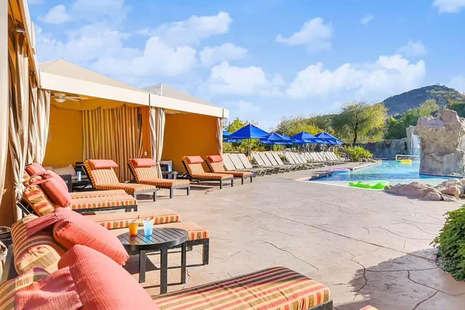 Luxurious poolside area with orange cabanas, striped loungers, blue umbrellas, and mountain views