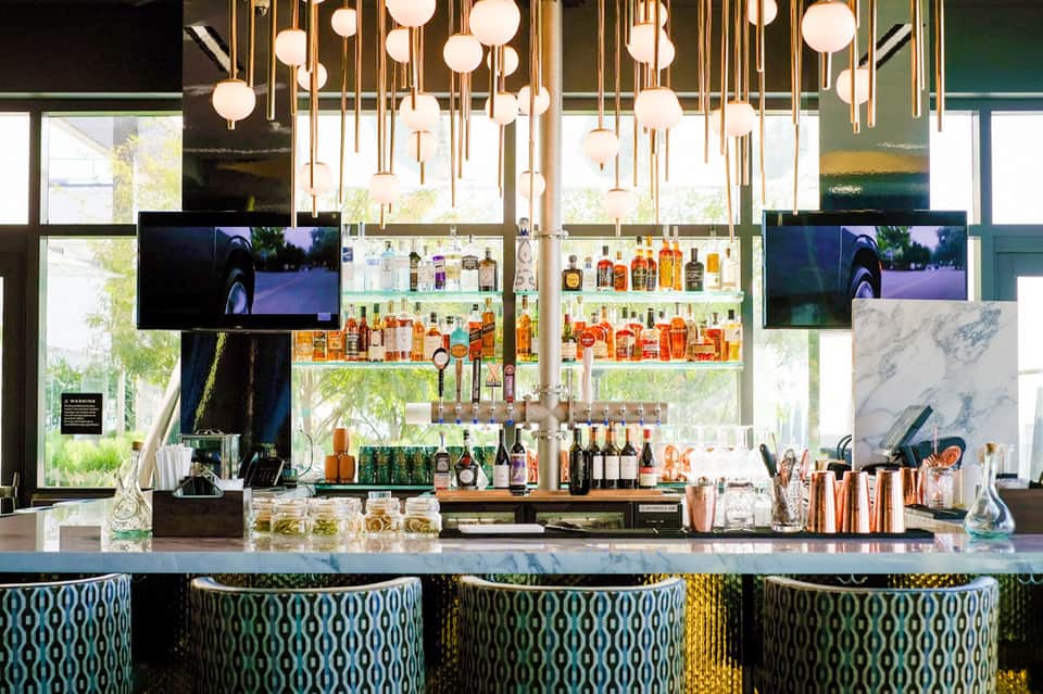 Modern bar with shelves of spirits, hanging globe lights, and patterned bar stools