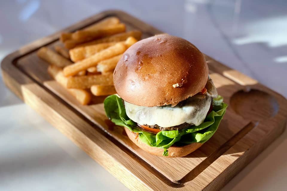 Gourmet burger with lettuce and cheese served with French fries on wooden board