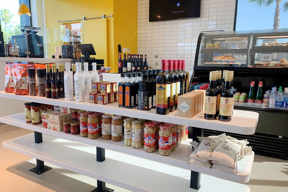 Gourmet deli counter displaying wines, oils, pastas, and specialty foods in a bright coastal resort shop