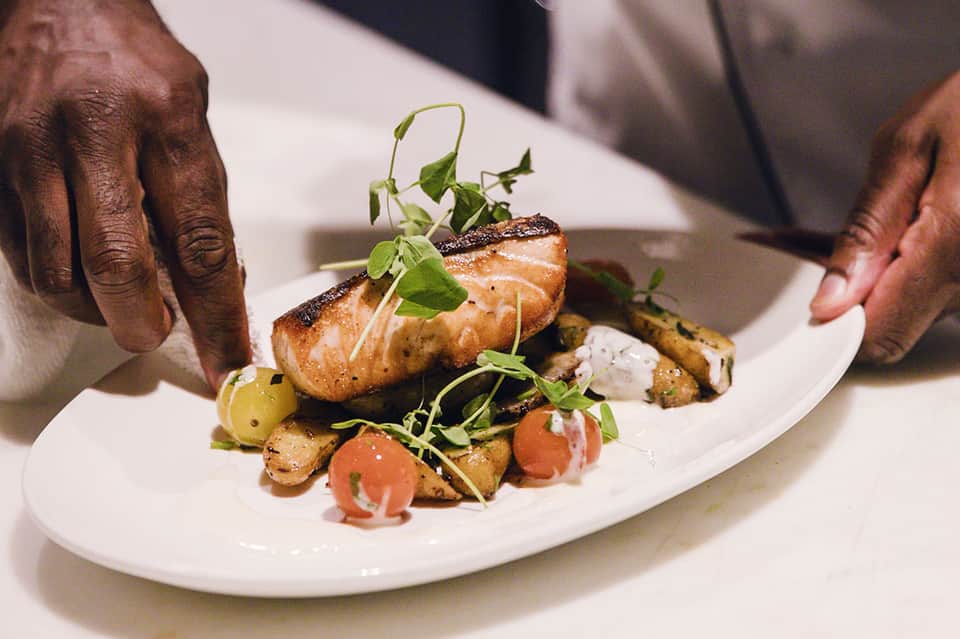 Chef presenting plated salmon dish with roasted vegetables and microgreens