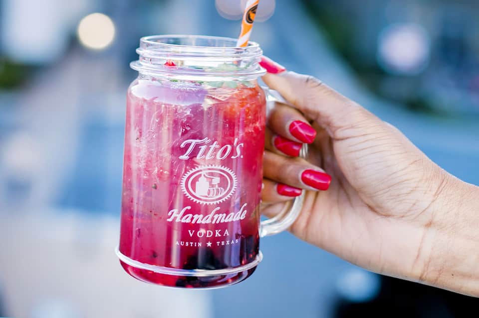 Pink cocktail with vodka in branded mason jar held by person with pink nail polish