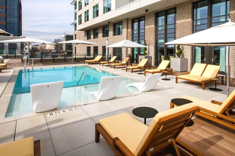 Resort pool deck with loungers, umbrellas, and brick building with yellow cushioned seating