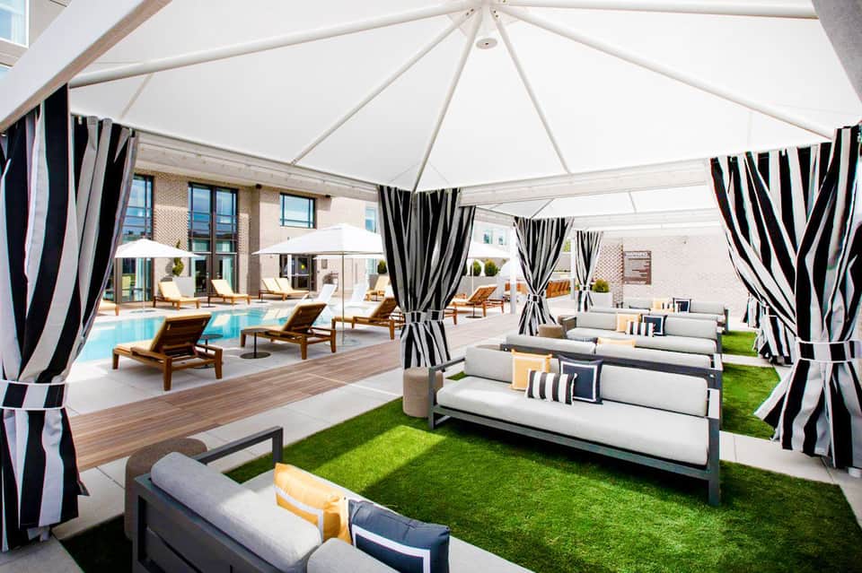Modern rooftop pool deck with striped cabanas, loungers, and white tent canopies overlooking a building