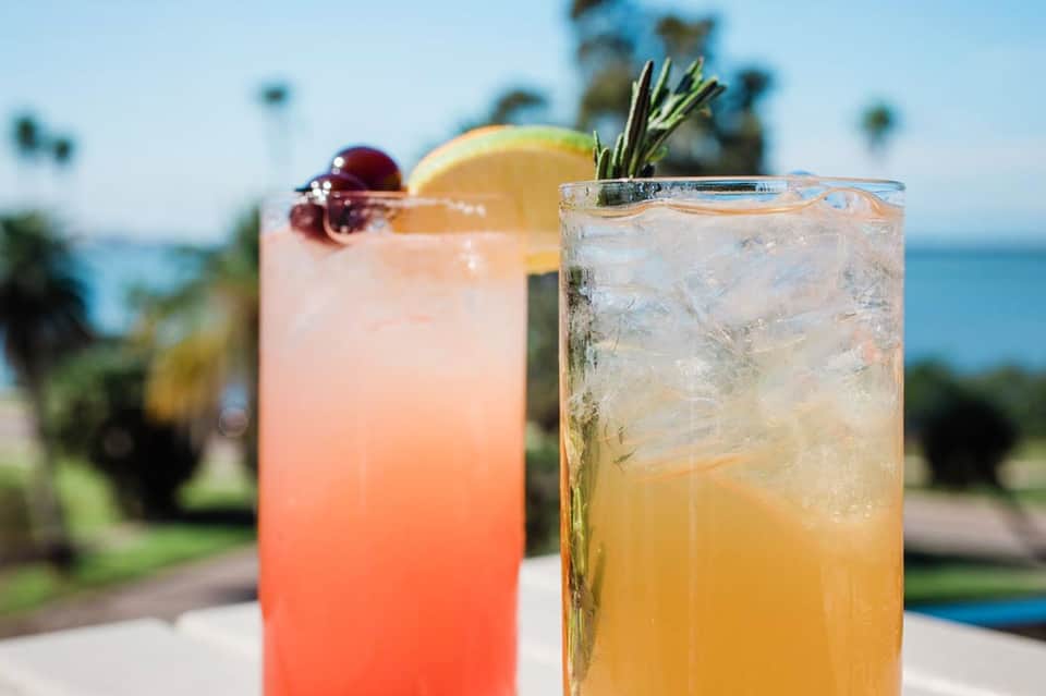 Two colorful cocktails with citrus garnish overlooking a coastal landscape with palm trees