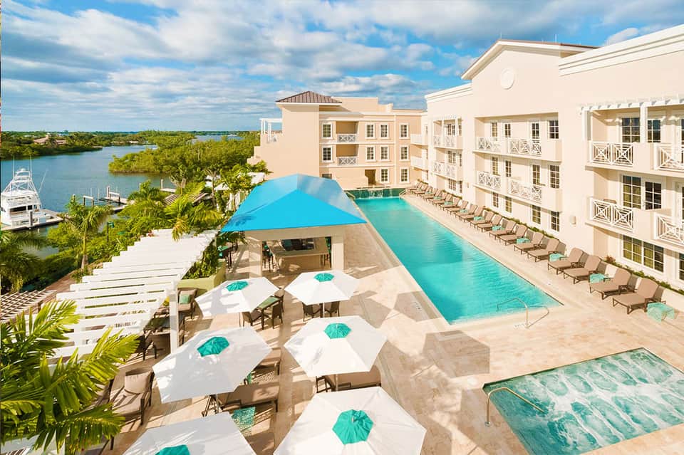Beige resort building with turquoise infinity pool overlooking waterway with boats and mangrove trees