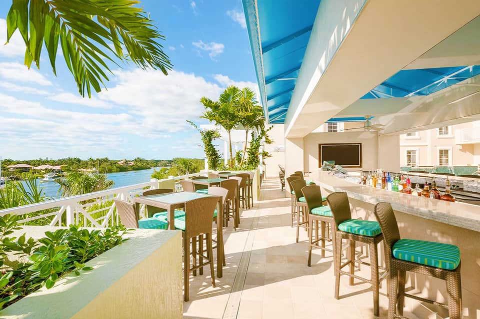Waterfront bar and patio with wicker seating, turquoise water views, and tropical landscaping